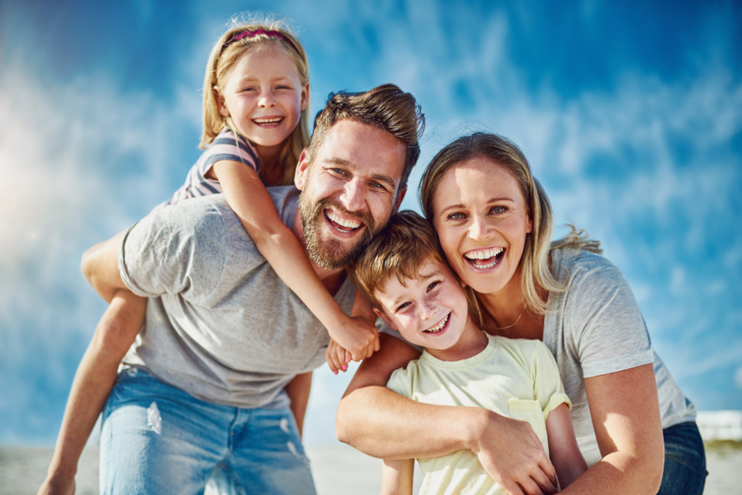 habits of happy people Joyful family smiling together outdoors under a clear blue sky, illustrating the habits of happy people.