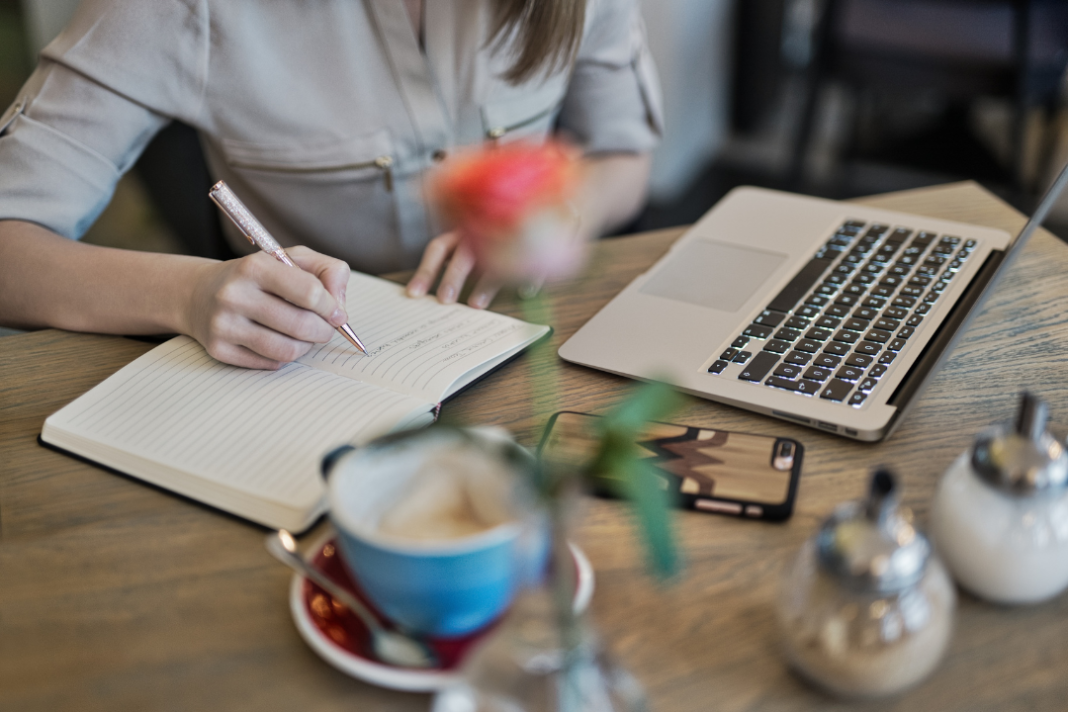 Woman journaling beside a laptop and coffee, practicing life-changing daily habits for focus and personal growth.